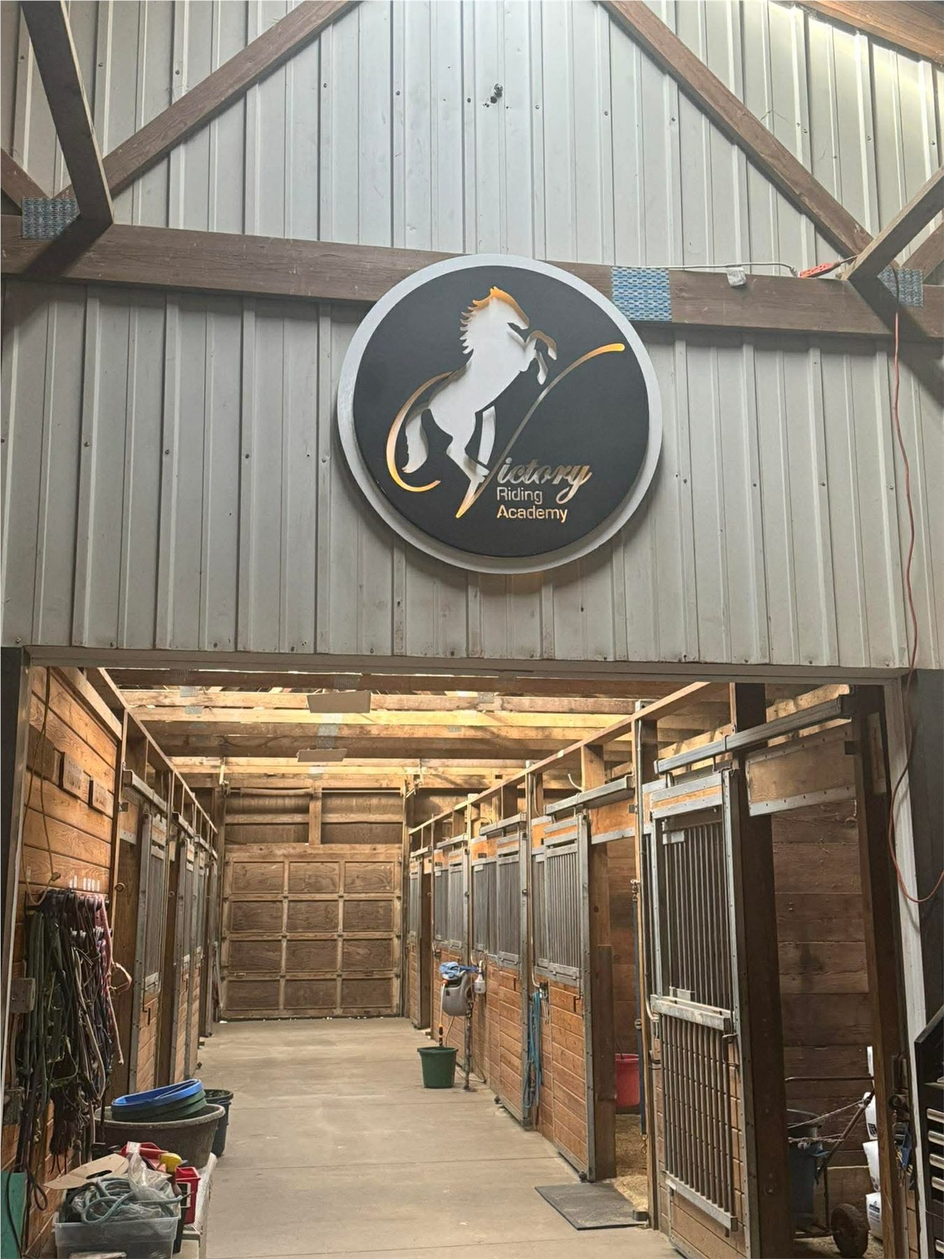 Round custom metal Victory Riding Academy sign installed inside a horse barn